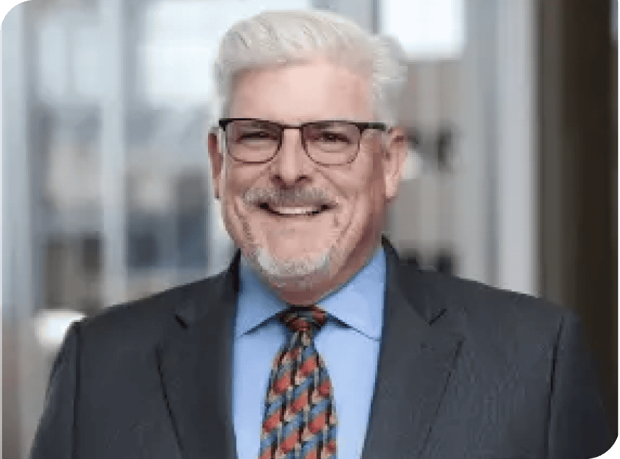 Business professional smiling in formal attire with glasses, standing outdoors in an urban setting.