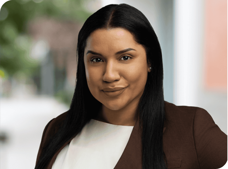 Business professional woman with dark hair in a brown blazer, smiling confidently outdoors.