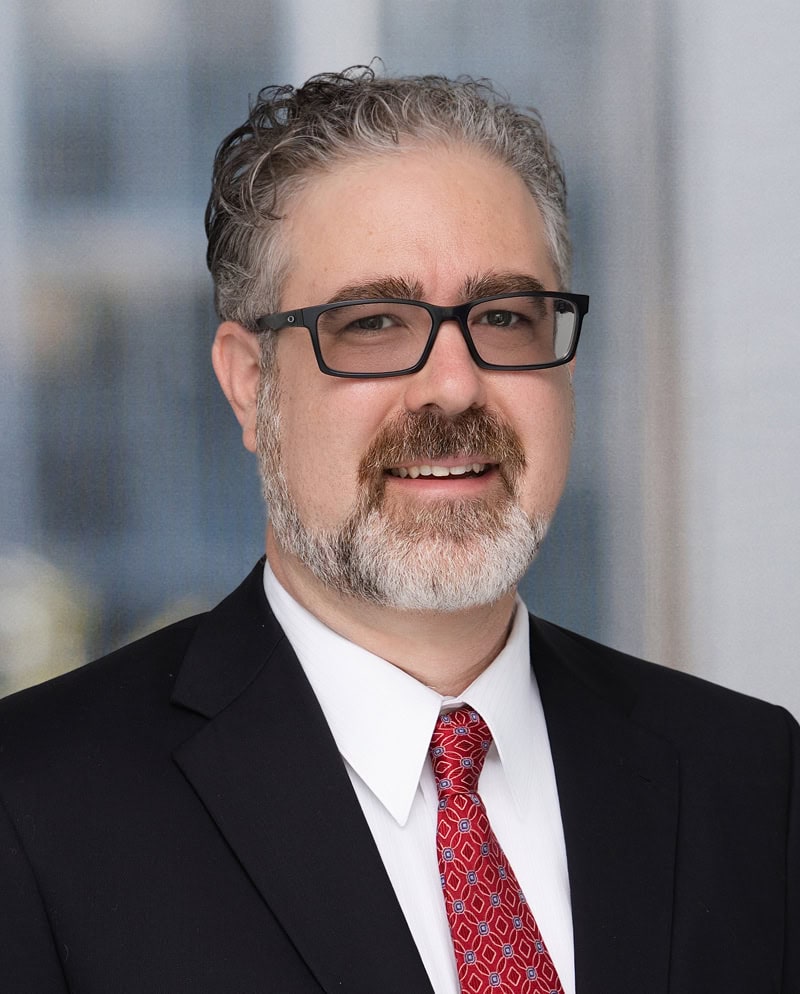 Portrait of Adam Wall in business attire with glasses and a friendly smile.
