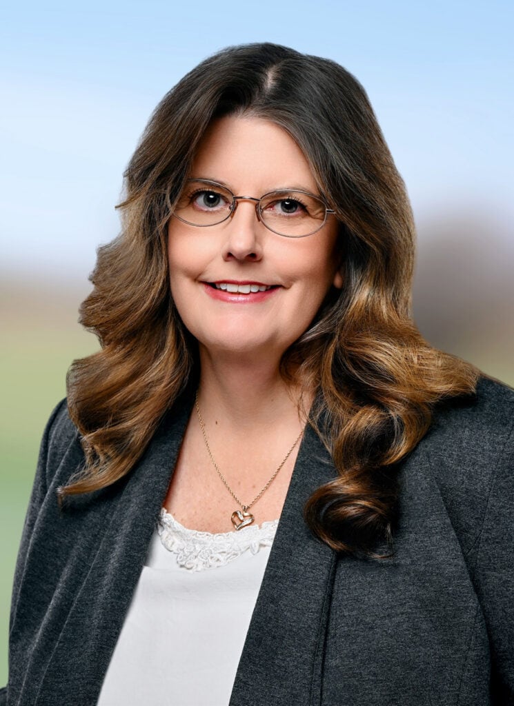 Professional woman with glasses smiling outdoors in business attire.