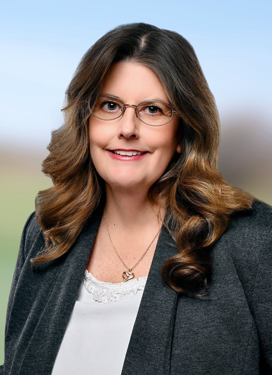 Professional woman with glasses smiling outdoors in business attire.