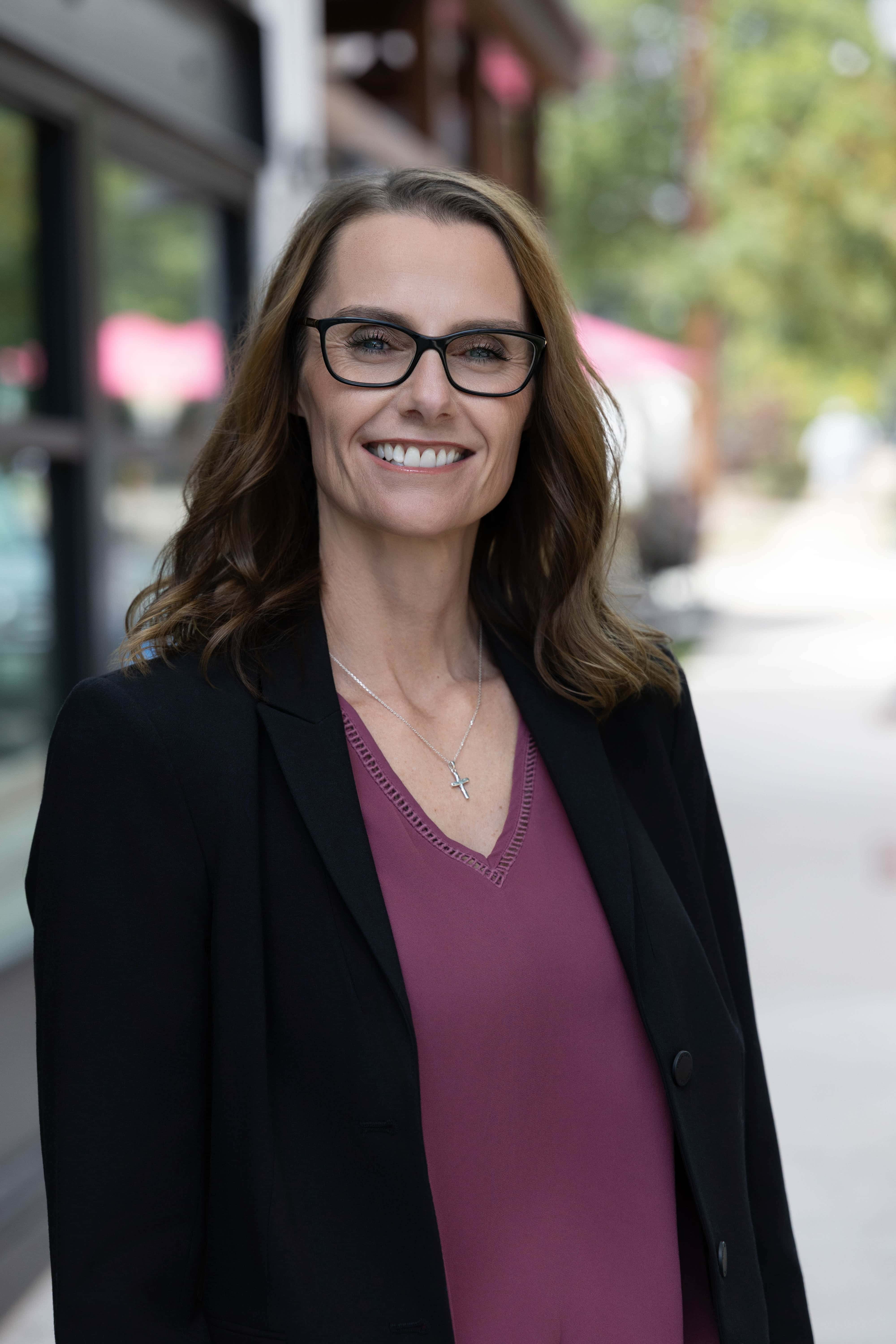 Professional woman with glasses smiling outdoors in business attire.