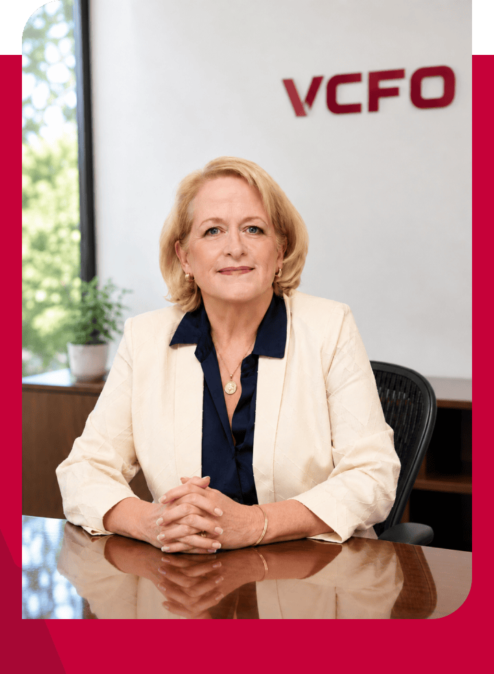 Professional woman sitting at desk in VCFO office with logo in background.