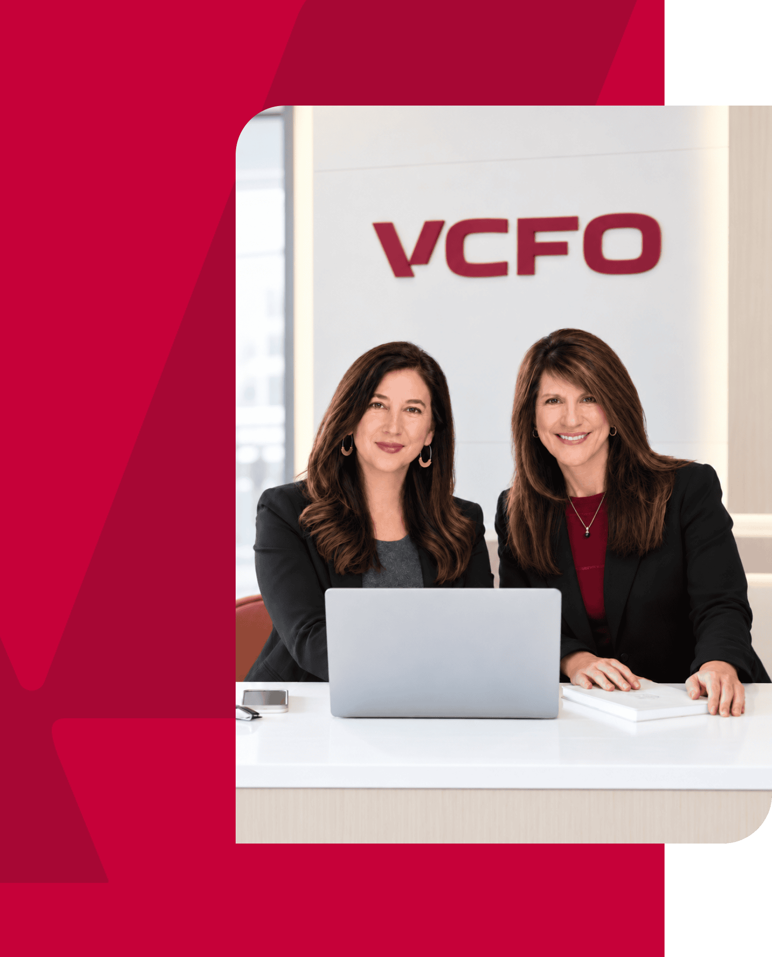 Two women in professional attire at a desk with a laptop, VCFO logo in background.