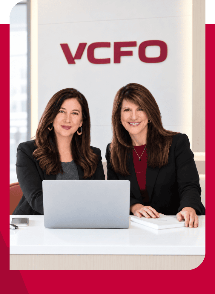 Two professional women at VCFO office with laptop and documents.