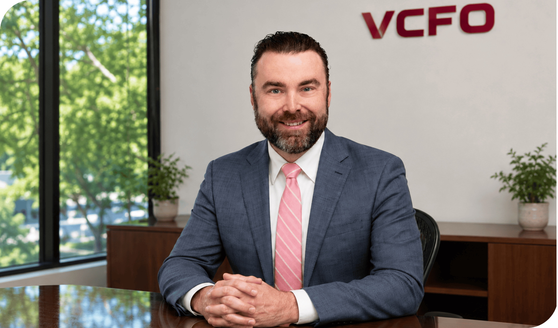 Professional man in a suit sitting at a desk in an office with VCFO logo.