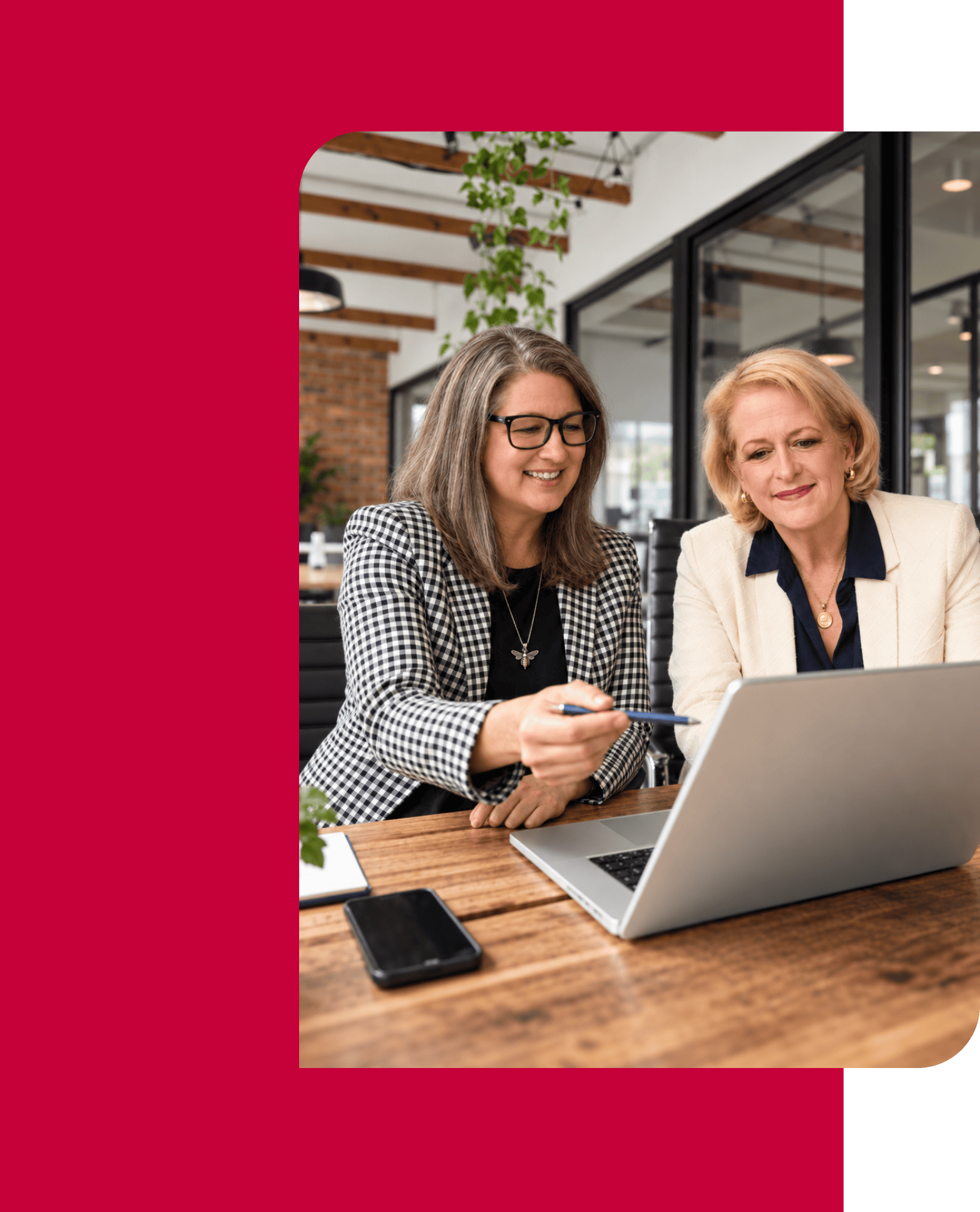 Two women collaborating on a laptop in a modern office setting.
