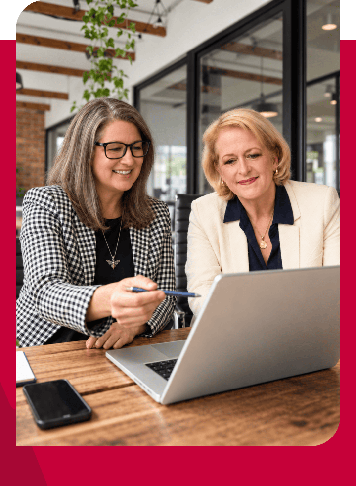 Two professional women collaborating on a laptop in a modern office setting.